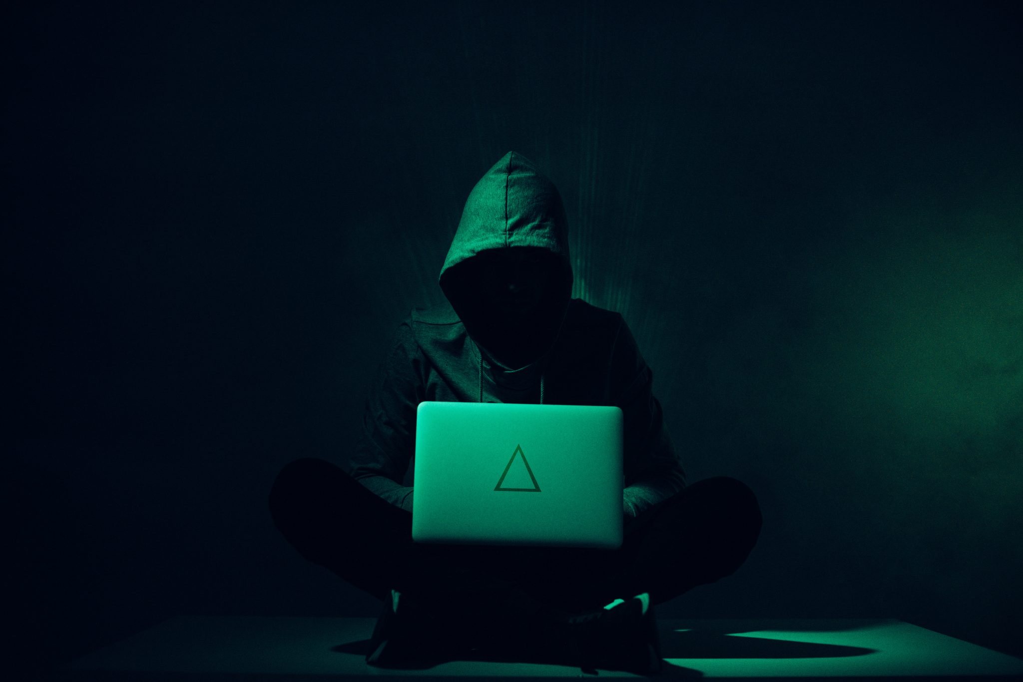 toned picture of silhouette of hacker in hoodie using laptop
