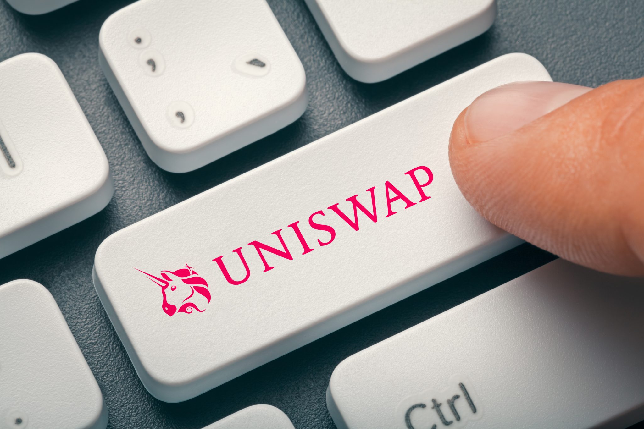 Male finger pressing computer key with uniswap | uni altcoin logo.  Cryptocurrrency mining or trading concept.