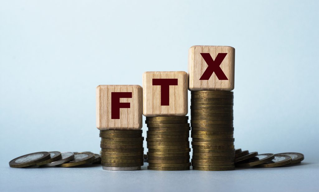 FTX - acronym on wooden cubes. Which stand on stacks of coins on a light background. Business concept