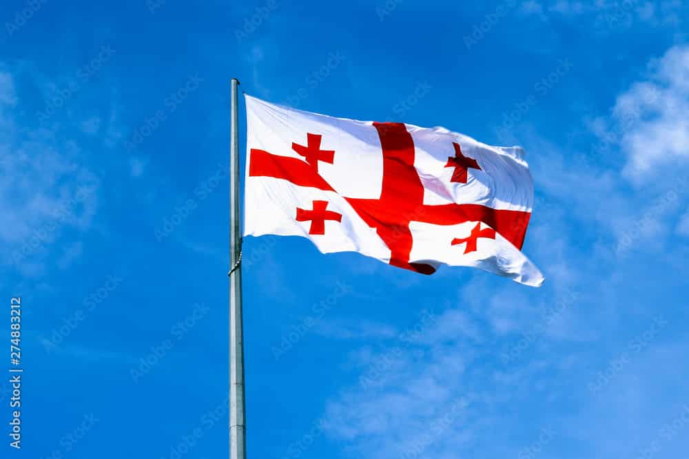 Waving Georgian flag and blue sky with clouds on background