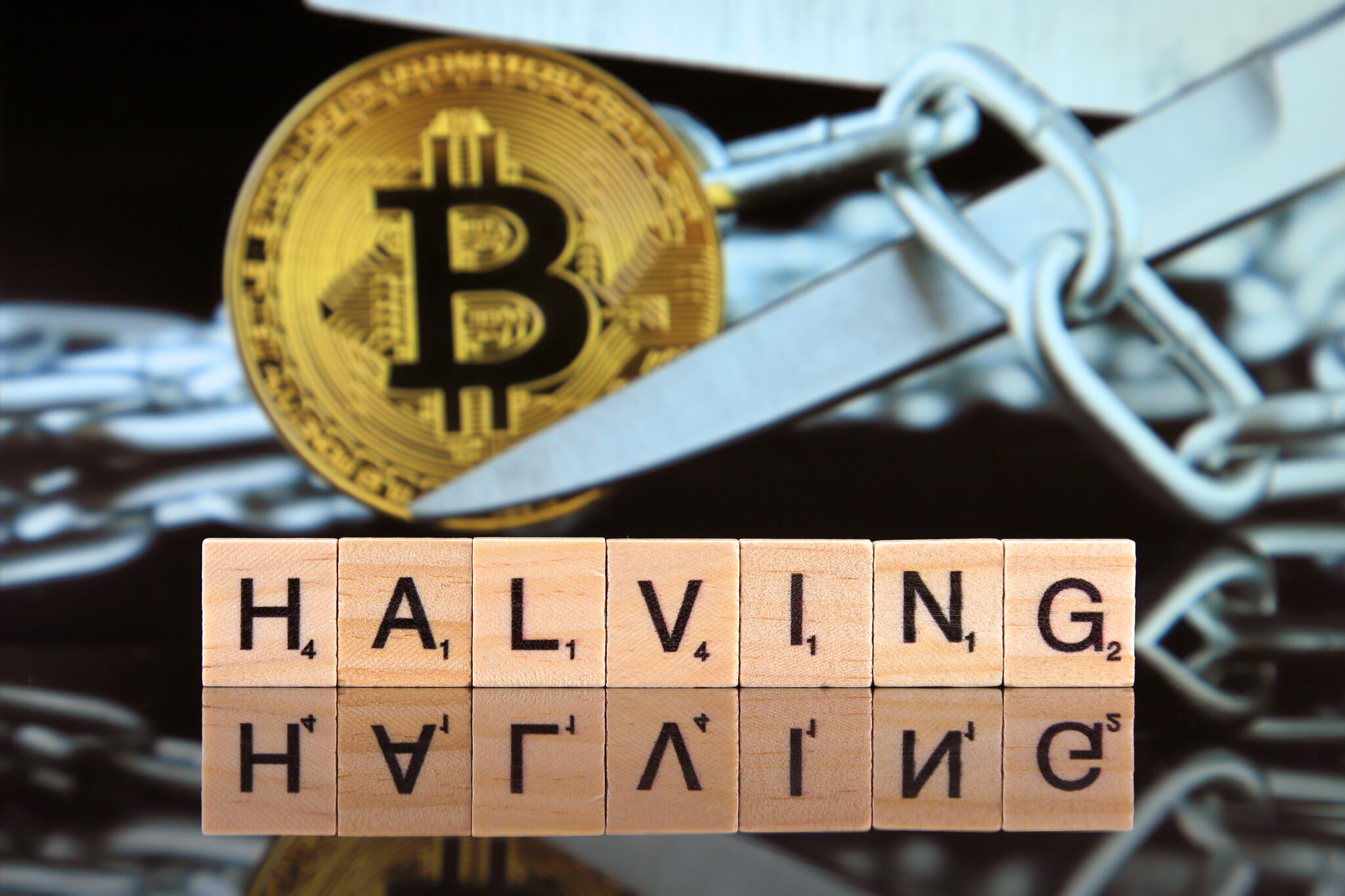 WROCLAW, POLAND - FEBRUARY 28, 2020: The word HALVING made of scrabble letters, physical version of Bitcoin and scissors in the background. Every 4 years the reward for adding a block is cut in half.