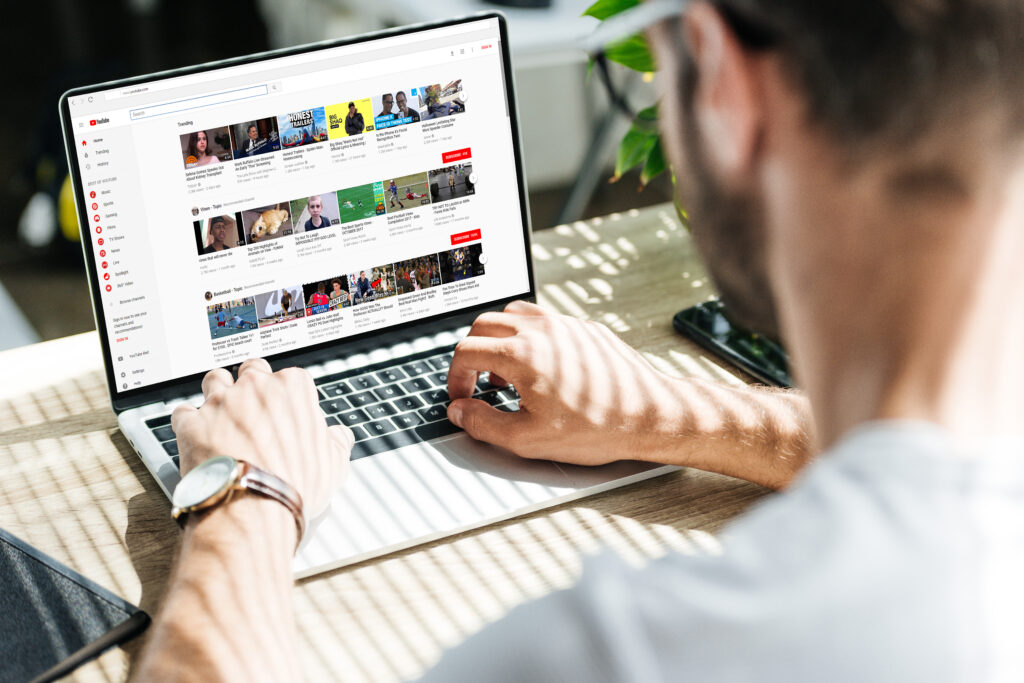 back view of man using laptop with youtube website on screen