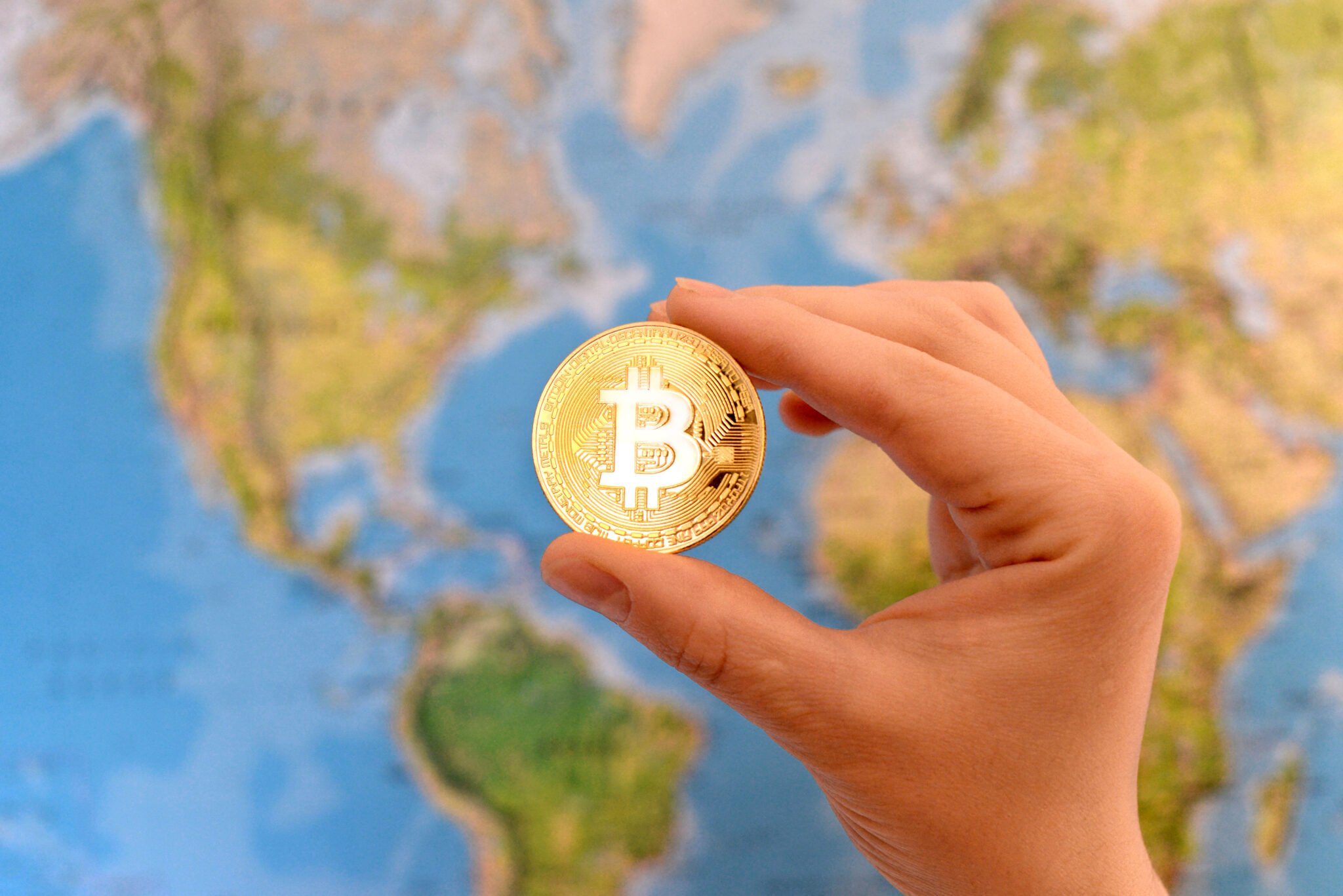 Hand holding gold coin of Bitcoin against map of world.