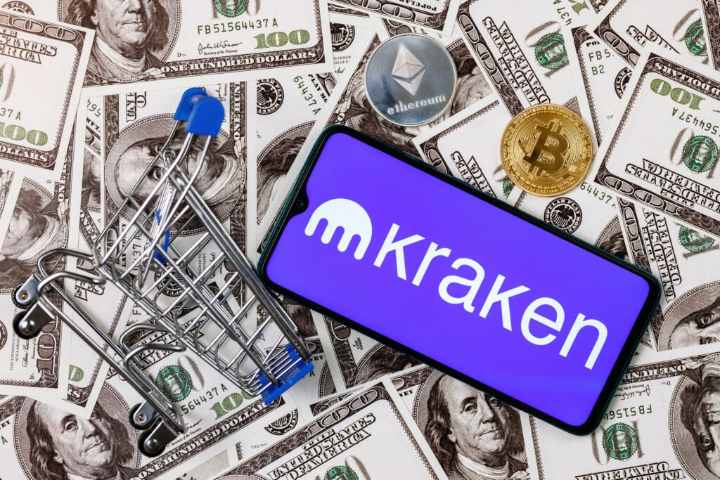 Kazan, Russia - Oct 12, 2021: Kraken is cryptocurrency exchange. A smartphone with the Kraken logo, a shopping cart and a cryptocoins on the dollar bills.