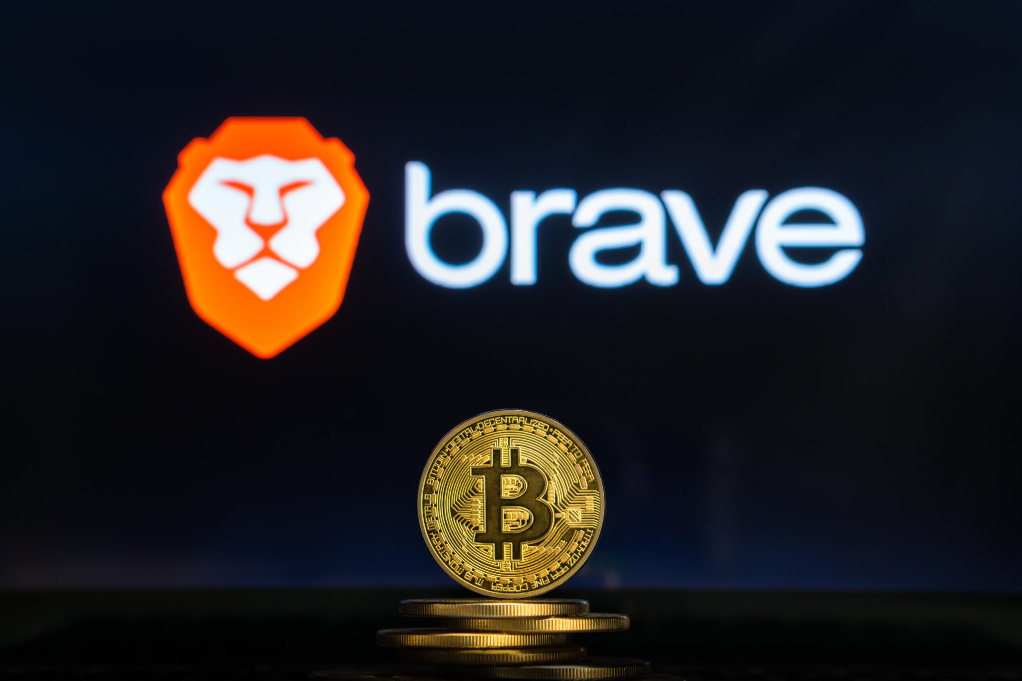 Brave logo on a computer screen with a stack of Bitcoin cryptocurency coins.