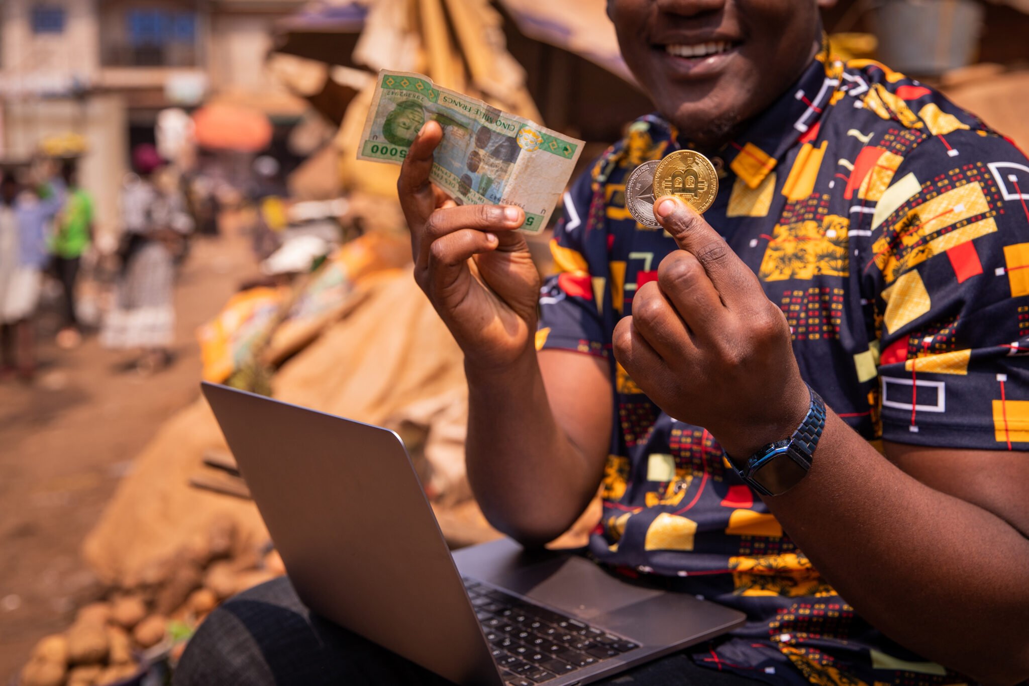 Close-up of the hands of an African boy holding a Bitcoin and Ethereum coin and a 5000 CFA franc note. Digital payments tin Africa concept