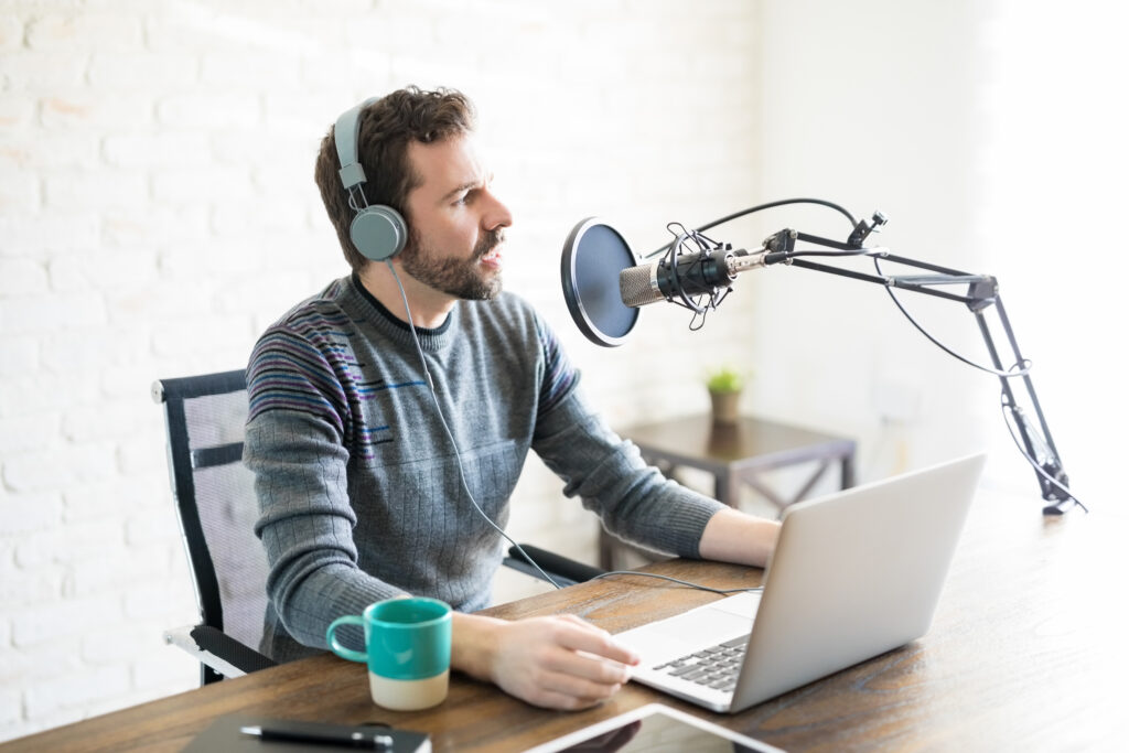 Hispanic young man with headphones and laptop talking on mic, online radio.