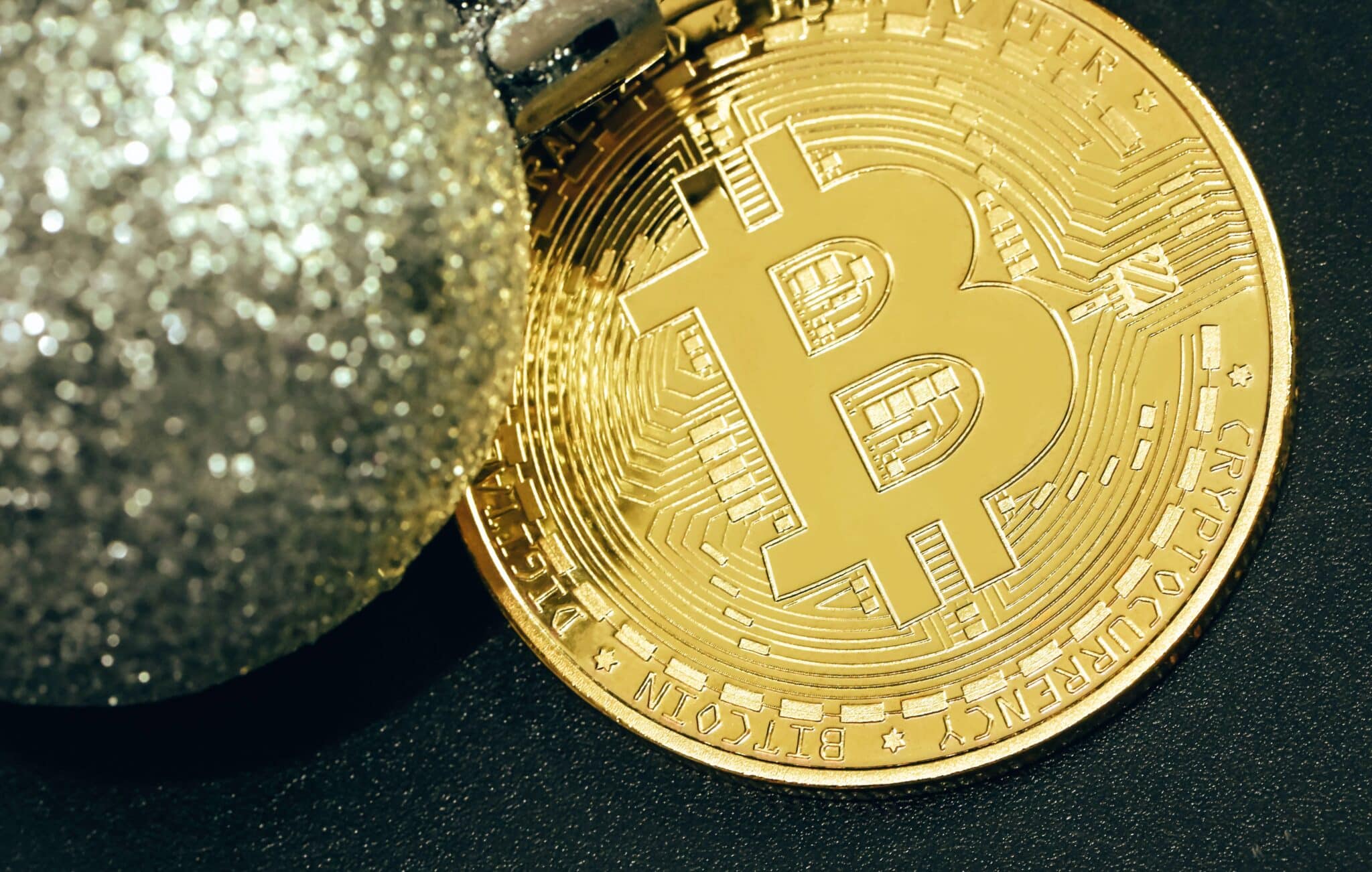 A gold Bitcoin placed next to a silver glitter Christmas ball