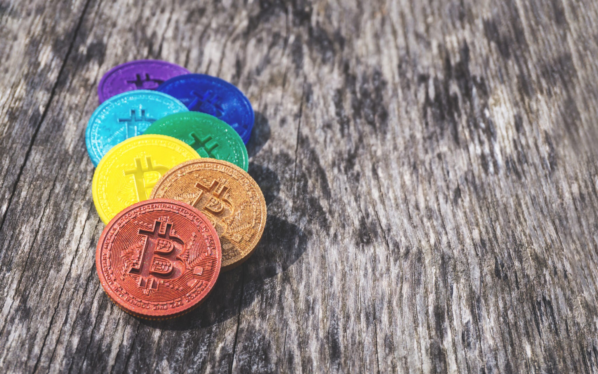 Colorful Bitcoin coins in rainbow colors on weathered wood with copy space