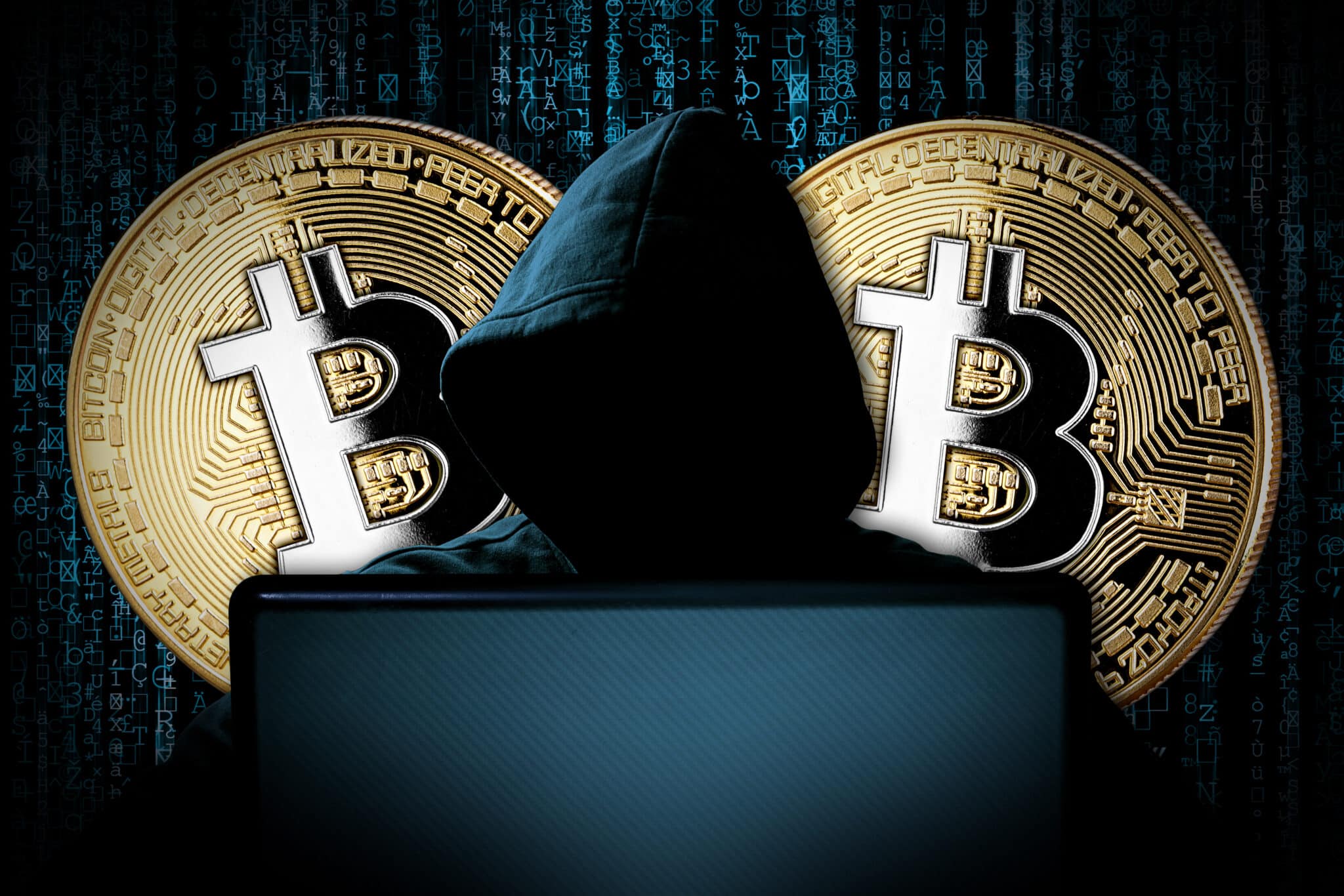 Une personne portant une capuche et dont le visage est caché sous l'ombre, devant un ordinateur portable portant. Deux tokens bitcoin apparaissent derrière elle.