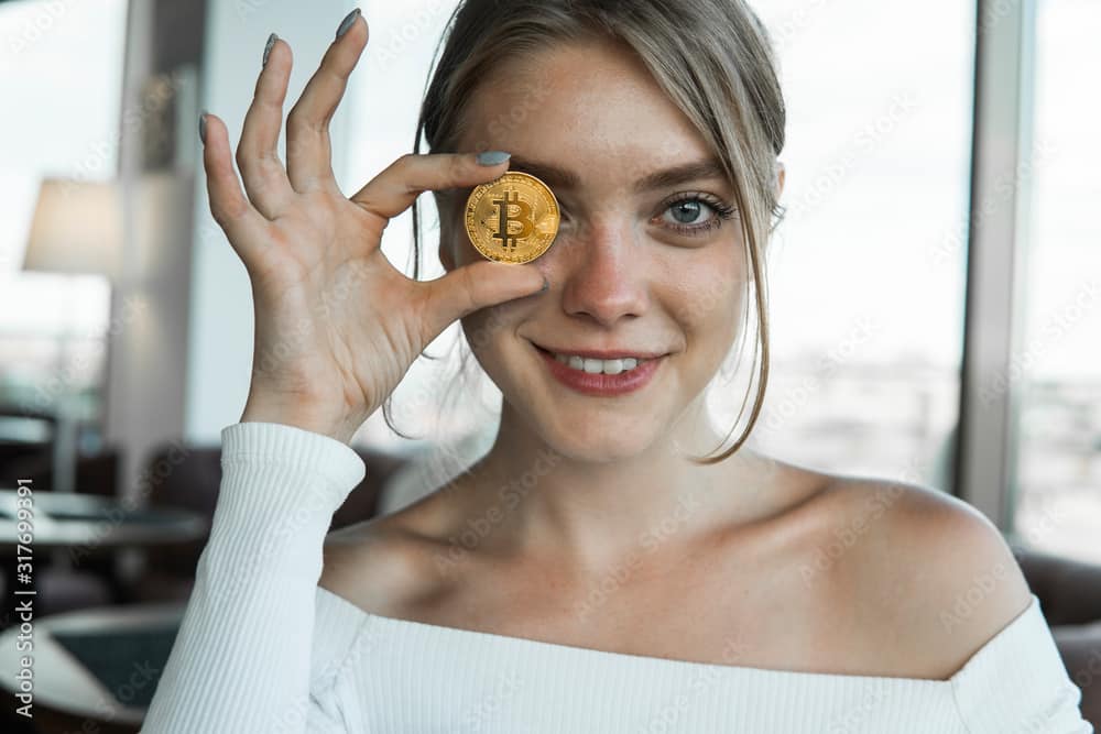 Close up fun emotional young female is holding bitcoin in forehead eye.  Online virtual future currency concept.  Beauty woman head with bitcoin money in eye.  Digital cryptocurrency bitcoin.
