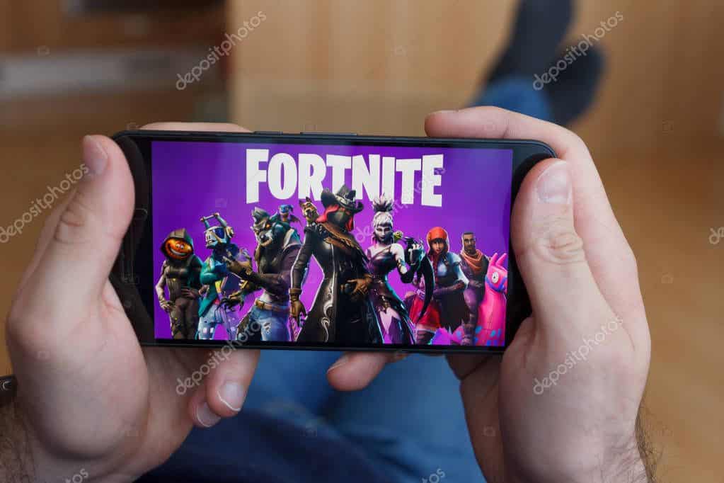 LOS ANGELES, CALIFORNIA - JUNE 3, 2019: Lying Man holding a smartphone and playing the Fortnite game on the smartphone screen. An illustrative editorial image.