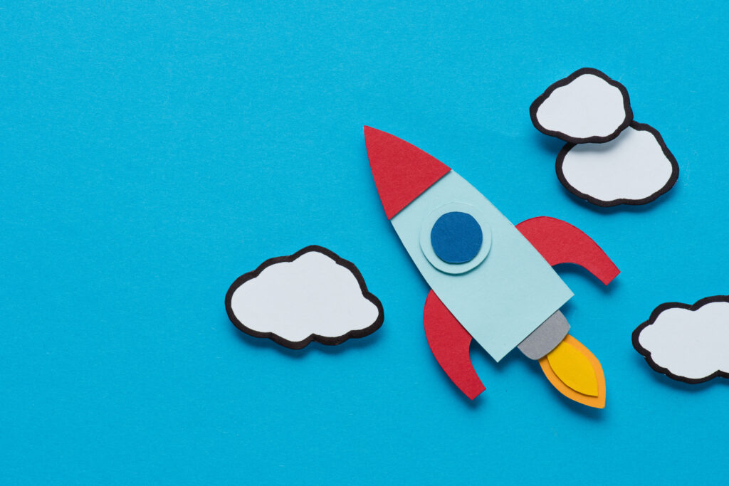 top view of cardboard rocket with clouds on blue background, setting goals concept