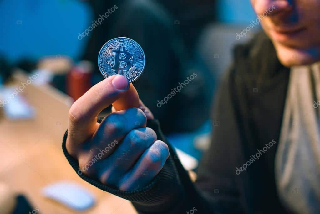 cropped shot of hacker holding bitcoin in dark room