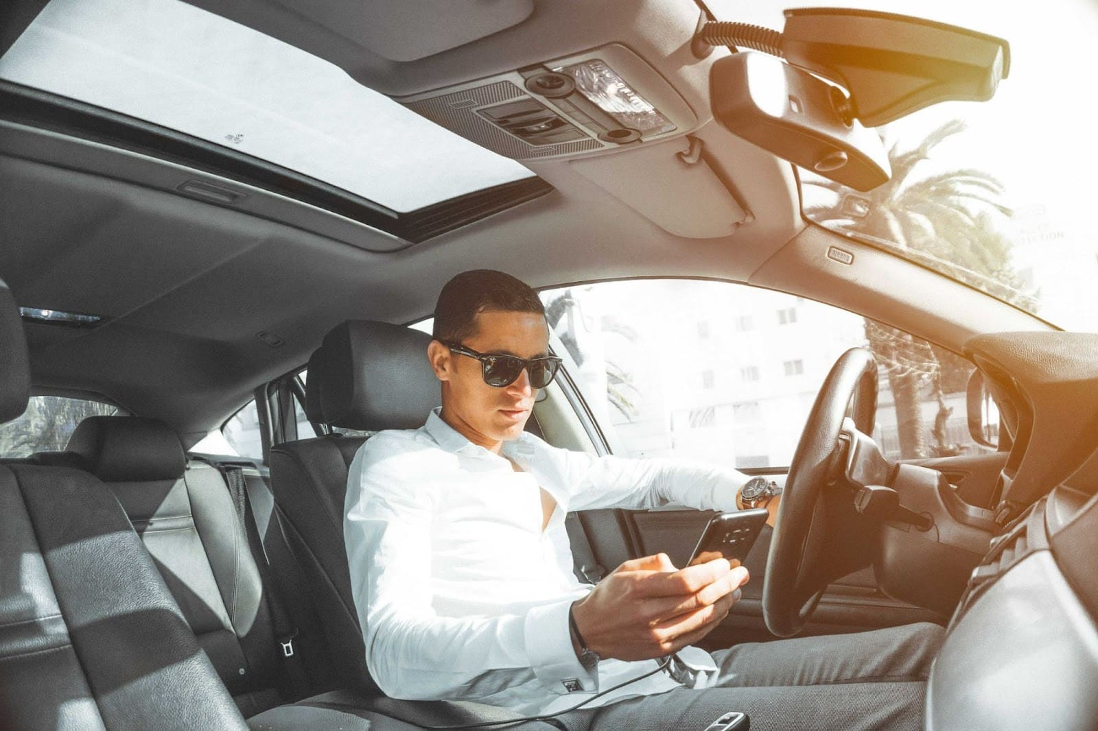 Un homme dans une voiture de luxe en train d'utiliser son téléphone portable.
