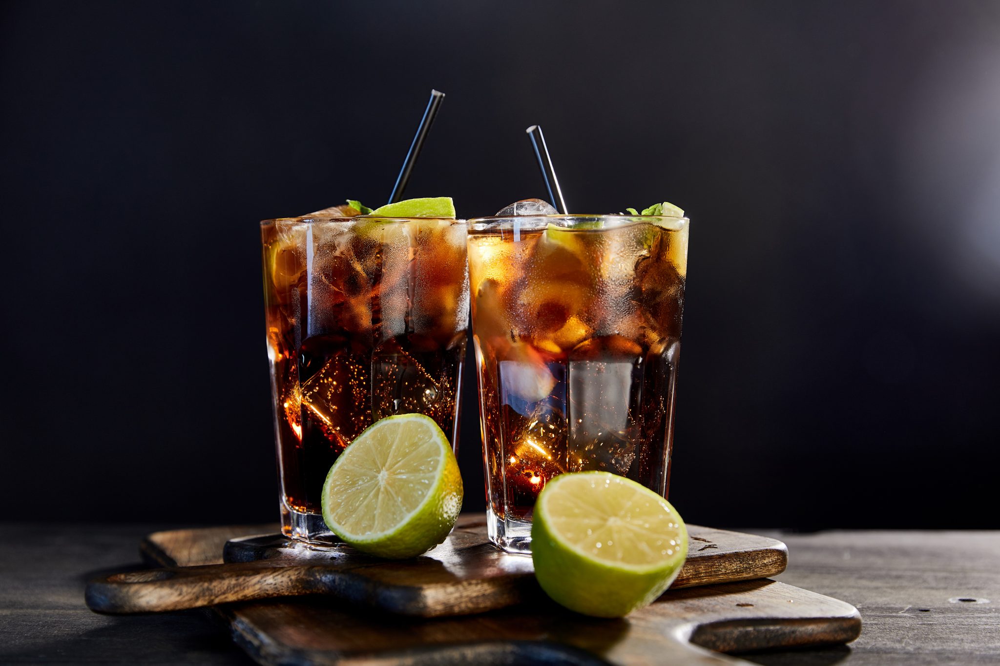 cocktails cuba libre in glasses with straws and limes on black background