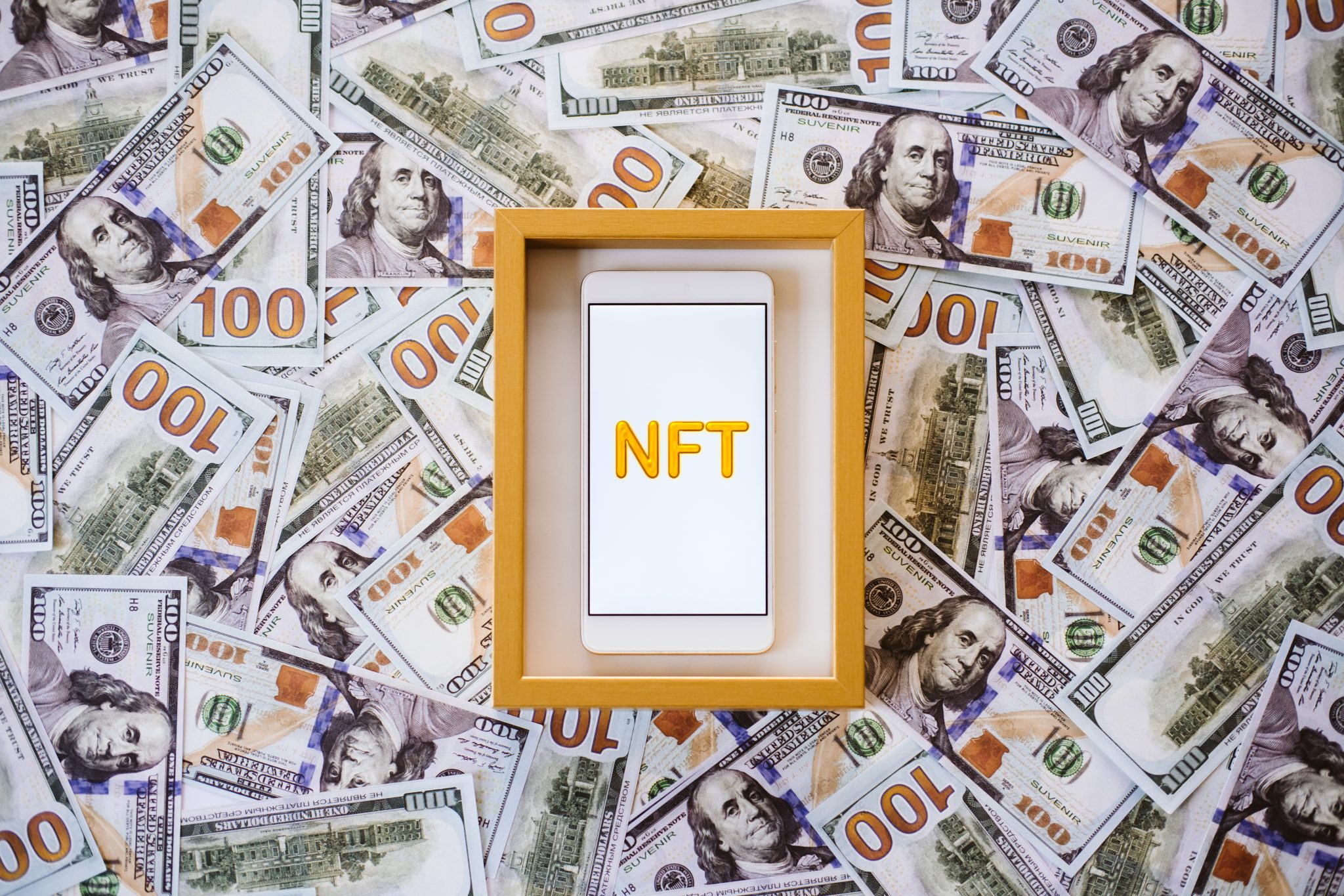 Non-fungible token NFT, crypto art, digital art, new type of cryptorurrency. Cell phone with golden NFT text in golden frame as art object on dollars background